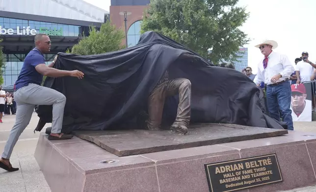 Former Texas Rangers player Adrian Beltre, left, and artist Mike Tabor, right, unveil a statue of Beltre before a baseball game between the Cleveland Guardians and the Rangers, Friday, Aug. 22, 2025, in Arlington, Texas. (AP Photo/LM Otero)