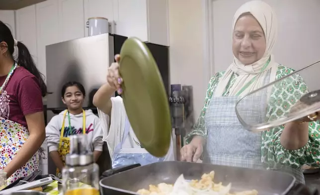 Shameem Syed, right, teaches students how to make a chicken stir fry during a cooking class at Olive Community Services, Tuesday, July 29, 2025, in Fullerton, Calif. The class was part of the organization's Intergenerational Summer Camp. (AP Photo/Zoë Meyers)