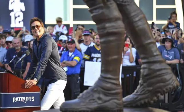 Former New England Patriots quarterback Tom Brady, left, looks at a bronze statue of himself after it was unveiled in Patriot Place Plaza before an NFL preseason football game between the Washington Commanders and the New England Patriots Friday, Aug. 8, 2025, in Foxborough, Mass. (AP Photo/Charles Krupa)