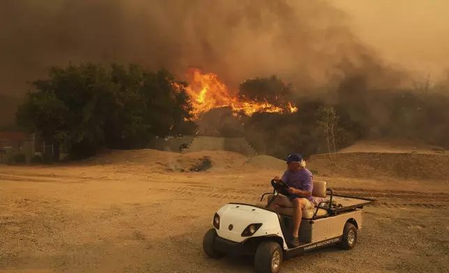 A resident rides a golf cart as he exits his property while the Canyon Fire burns on Thursday, Aug. 7, 2025, in Halsey Canyon, Calif. (AP Photo/Marcio Jose Sanchez)