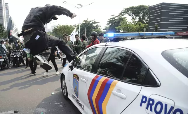 A student attacks a police car during a protest following the death of a delivery rider who was run over by a police armored vehicle in a rally against lawmakers' privilege, in Jakarta, Indonesia, Friday, Aug. 29, 2025. (AP Photo/Tatan Syuflana)