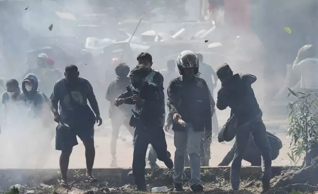 People react as police fire tear gas during a protest following the death of a delivery rider who was run over by a police armored vehicle in a rally against lawmakers' privilege, in Jakarta, Indonesia, Friday, Aug. 29, 2025. (AP Photo/Achmad Ibrahim)