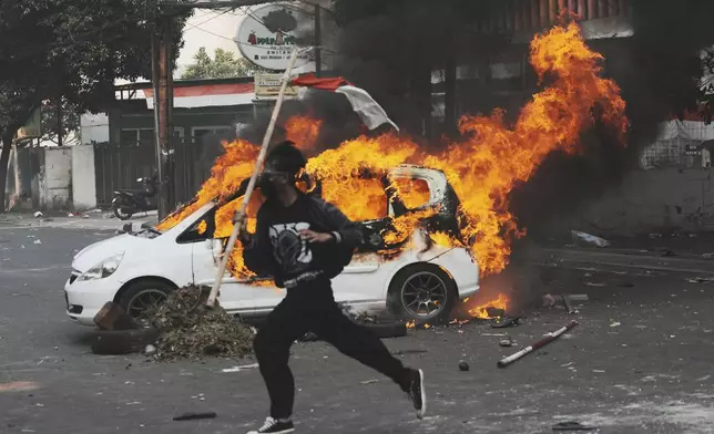 A protester runs past a burning car during a protest following the death of a delivery rider in clashes between riot police and students protesting against lawmakers' allowances, in Jakarta, Indonesia, Friday, Aug. 29, 2025. (AP Photo/Achmad Ibrahim)