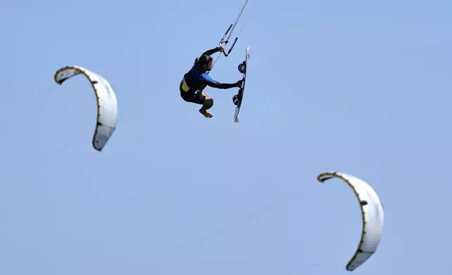 Kiteboarder Alexios Limperopoulos performs a jump during a windy day in Agios Nikolaos Artemida, east of Athens, Greece, Thursday, Aug. 7, 2025. (AP Photo/Thanassis Stavrakis)