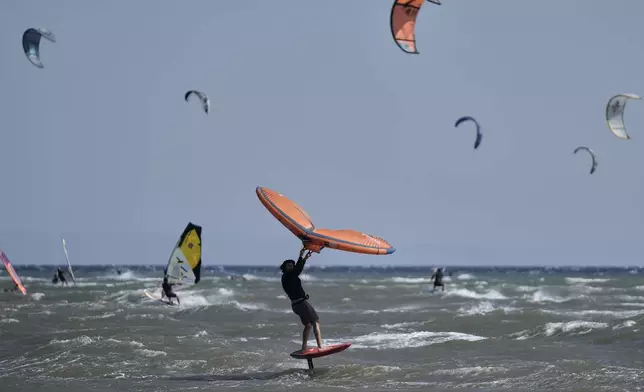 A wingfoiler skips over waves on a windy day in Agios Nikolaos Artemida, east of Athens, Greece, Thursday, Aug. 7, 2025. (AP Photo/Thanassis Stavrakis)