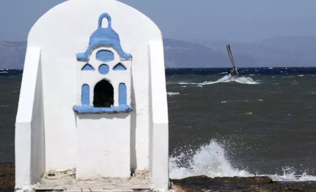 A windsurfer skips over a wave on a windy day in Agios Nikolaos Artemida, east of Athens, Greece, Thursday, Aug. 7, 2025. (AP Photo/Thanassis Stavrakis)