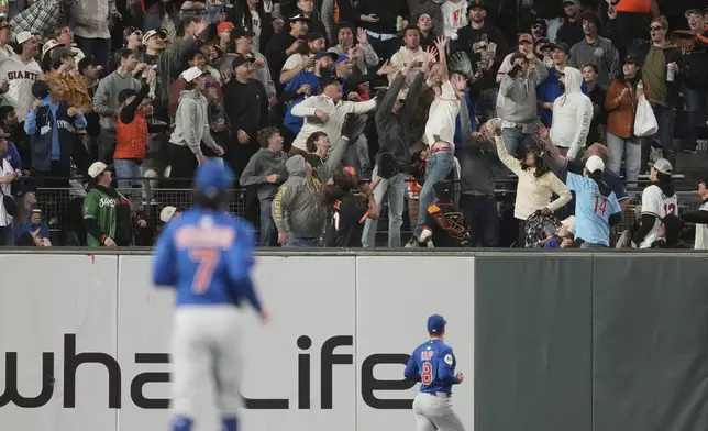Chicago Cubs shortstop Dansby Swanson, foreground, and left fielder Ian Happ (8) watch as fans reach for a two-run home run hit by San Francisco Giants' Matt Chapman during the sixth inning of a baseball game in San Francisco, Tuesday, Aug. 26, 2025. (AP Photo/Jeff Chiu)