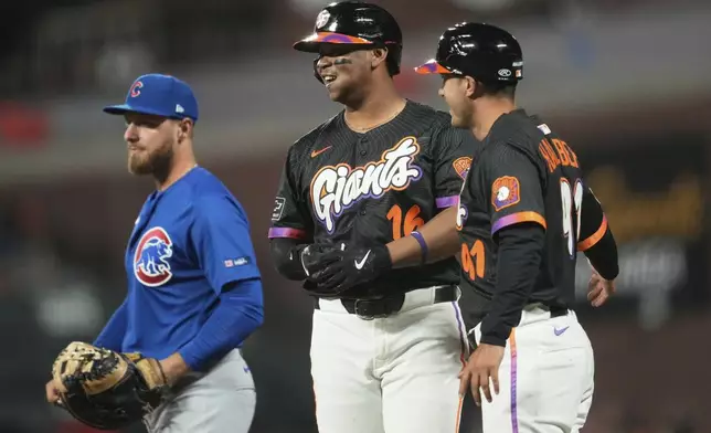 San Francisco Giants' Rafael Devers, middle, reacts after hitting an RBI single between first base coach Mark Hallberg, right, and Chicago Cubs first baseman Michael Busch during the fifth inning of a baseball game in San Francisco, Tuesday, Aug. 26, 2025. (AP Photo/Jeff Chiu)