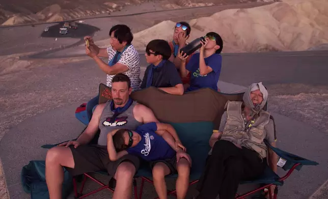 Joe Chyuwei, right, Addison Black, front center, James Black, front left, and back row from left, Helen Chyuwei, Jameson Black, Grace Chyuwei and Grayson Black watch the sunset in the heat at Zabriskie Point, Sunday, Aug. 3, 2025, in Death Valley National Park, Calif. (AP Photo/John Locher)
