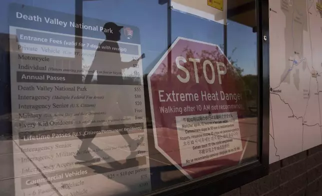 A person walks by a sign warning of extreme heat danger at the Furnace Creek Visitor Center, Sunday, Aug. 3, 2025, in Death Valley National Park, Calif. (AP Photo/John Locher)