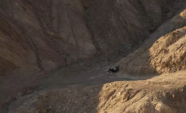A hiker rests in the shade near Zabriskie Point, Sunday, Aug. 3, 2025, in Death Valley National Park, Calif. (AP Photo/John Locher)