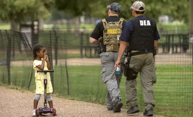 A child watches as officers with the Drug Enforcement Administration patrol along the National Mall Wednesday, Aug. 13, 2025, in Washington. (AP Photo/Mark Schiefelbein)