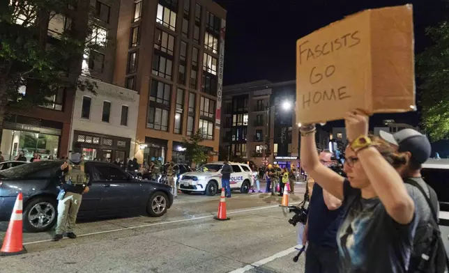 A person holds a sign as Department of Homeland Security Investigations agents join Washington Metropolitan Police Department officers as they conduct traffic checks at a checkpoint along 14th Street in northwest Washington, Wednesday, Aug. 13, 2025, in Washington. (AP Photo/Jose Luis Magana)