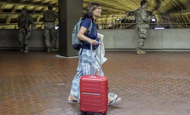 A woman rolls her suitcase past as District of Columbia National Guardsmen patrol inside the Gallery Place-Chinatown Metro Station, Sunday, Aug. 17, 2025, in Washington. (AP Photo/Julia Demaree Nikhinson)