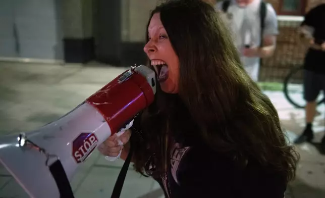 An unidentified woman screams at FBI agents through a bullhorn after they assisted U.S. Secret Service police taking a man into custody for allegedly possessing illegal drugs, near a homeless encampment in downtown Washington, Thursday, Aug. 14, 2025. (AP Photo/Cliff Owen)