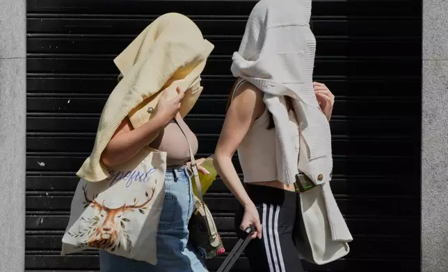 Two women walk with their heads covered to protect from the sun during extreme hot weather in Madrid, Spain, Sunday, Aug. 17, 2025. (AP Photo/Paul White)