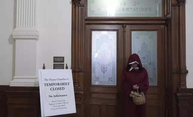 Sam Parker wears a "Handmaid's Tale" outfit as she stands outside of the House Chamber where Democratic Texas state Rep. Nicole Collier refuses to leave due to a required law enforcement escort, Tuesday, Aug. 19, 2025, in Austin, Texas. (AP Photo/Eric Gay)