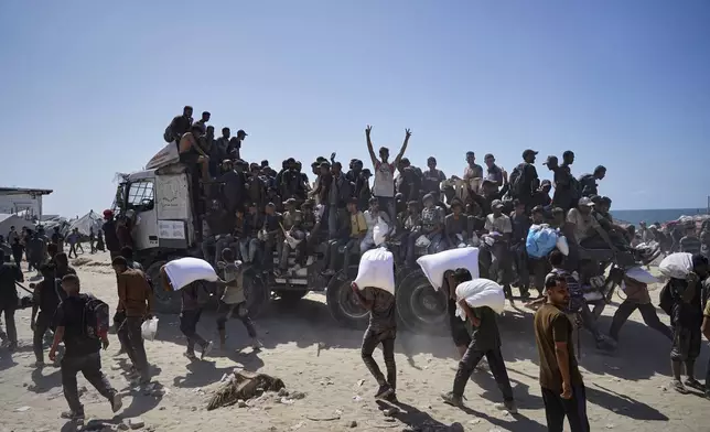 Palestinians carry sacks of flour taken from a humanitarian aid convoy en route to Gaza City, in the outskirts of Beit Lahiya, northern Gaza Strip, Friday, Aug. 1, 2025. (AP Photo/Jehad Alshrafi)