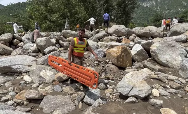 Rescue workers and local cross an area filled with rocks at after Friday's flash flood hit the area of Qadar Nagar in Buner district, in Pakistan's northwest, Monday, Aug. 18, 2025. (AP Photo/Mohammad Arif)