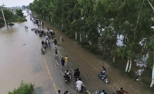 People wade through a flooded area after torrential rains along a highway on the outskirts of Narowal, Pakistan, Wednesday, Aug. 27, 2025. (AP Photo/Jahan Zab)
