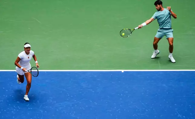 Carlos Alcaraz, right, of Spain, plays a shot as partner Emma Raducanu, of Great Britain, covers during their mixed doubles match at the U.S. Open tennis championships, Tuesday, Aug. 19, 2025, in New York. (AP Photo/Yuki Iwamura)