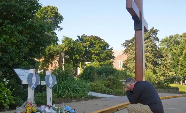 Dan Beazley kneels with a giant cross in front of a memorial at Annunciation Catholic Church after Wednesday's school shooting, Thursday, Aug. 28, 2025, in Minneapolis. (AP Photo/Abbie Parr)