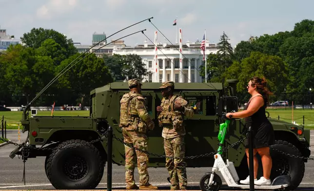Members of the District of Columbia National Guard patrol in front of the White House as a woman rides past on a scooter, Saturday, Aug. 16, 2025, in Washington. (AP Photo/Julia Demaree Nikhinson)