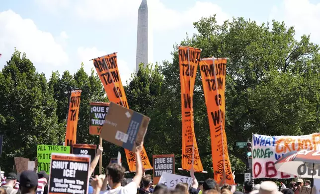 Activists carrying signs pass the Washington Monument as they march to the White House to protest President Donald Trump's federal takeover of policing of the District of Columbia, Saturday, Aug. 16, 2025, in Washington. (AP Photo/Alex Brandon)
