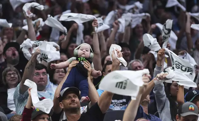 A fan holds up their baby as others wave towels during a Phoenix Mercury free throw against the Seattle Storm during the first half of a WNBA basketball game Sunday, Aug. 17, 2025, in Seattle. (AP Photo/Lindsey Wasson)