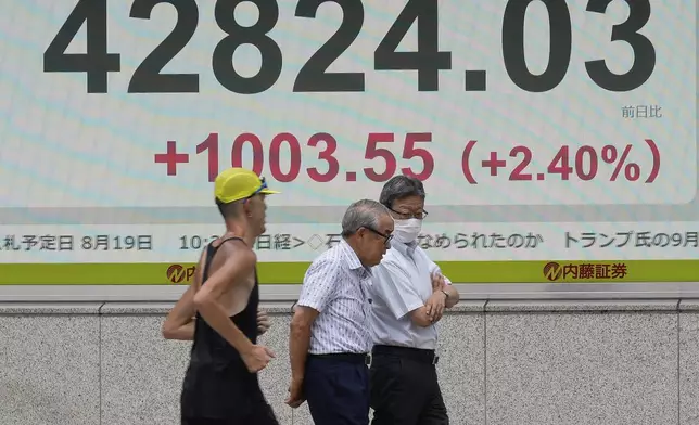People walk in front of an electronic stock board showing Japan's Nikkei index at a securities firm Tuesday, Aug. 12, 2025, in Tokyo. (AP Photo/Eugene Hoshiko)