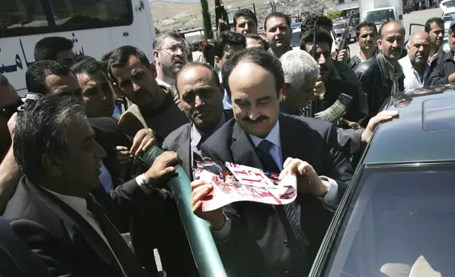 FILE - Then former head of the Syrian political security branch Maj. Gen. Rostom Ghazali, center, who also was a former Syrian intelligence chief in Lebanon, escorted by his supporters as he looks to an Arabic placard that reads:"Thanks Syria," after he get out from his car on his way cross the Lebanese border point of Masnaa in the Bekaa Valley, east of Beirut, Lebanon, April 26, 2005. (AP Photo/Hussein Malla, File)