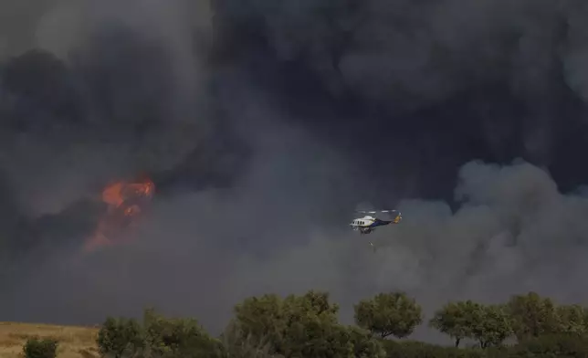 A helicopter flies through smoke from a fire at Keratea, outskirt of Athens, on Friday, Aug. 8, 2025. (AP Photo/Thanassis Stavrakis)