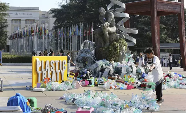 Benjamin Von Wong, right, a Canadian artist and activist, heaps piles of plastic waste onto a large sculpture that he designed in front of the United Nations office in Geneva, Switzerland, Monday, Aug. 11, 2025. (AP Photo/ Jennifer McDermott)
