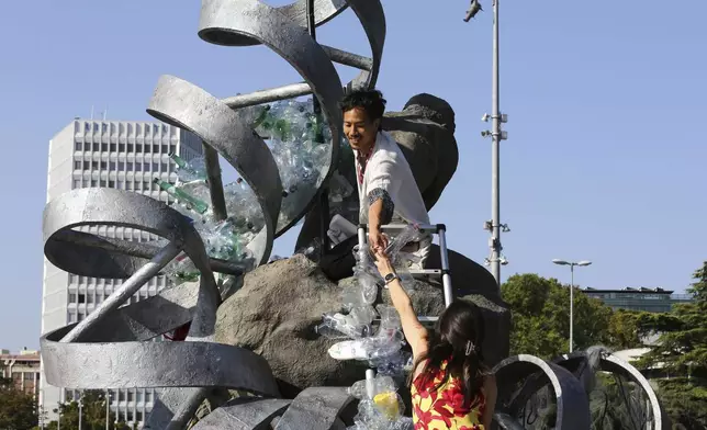 Benjamin Von Wong, top, a Canadian artist and activist, heaps piles of plastic waste onto a large sculpture that he designed in front of the United Nations office in Geneva, Switzerland, Monday, Aug. 11, 2025. (AP Photo/ Jennifer McDermott)