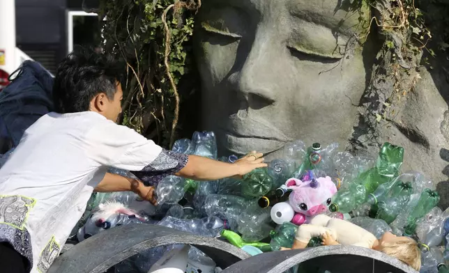 Benjamin Von Wong, a Canadian artist and activist, heaps piles of plastic waste onto a large sculpture that he designed in front of the United Nations office in Geneva, Switzerland, Monday, Aug. 11, 2025. (AP Photo/ Jennifer McDermott)