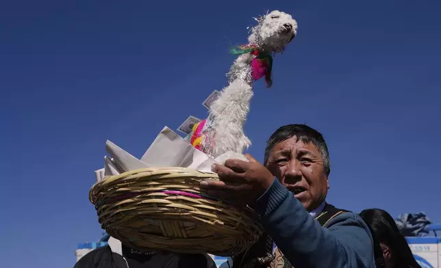 A spiritual leader holds a up a basket with a llama carcass to be burnt as an offering in observance of the month of Pachamama, or Mother Earth, performing an ancient tradition to ask for a good harvest, on the outskirts of La Paz, Bolivia, Friday, Aug. 1, 2025. (AP Photo/Juan Karita)