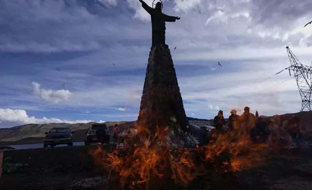 A statue of Jesus Christ towers over people burning offerings observing the month of Pachamama, or Mother Earth, performing an ancient tradition to ask for a good harvest, on La Cumbre, a mountain considered sacred on the outskirts of La Paz, Bolivia, Friday, Aug. 1, 2025. (AP Photo/Juan Karita)