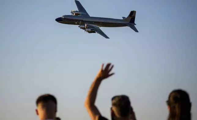 People wave as a Douglas DC-6B plane of the Flying Bulls Red Bull aerobatic team flies above the runway of the Aurel Vlaicu airport, on the first day of the Bucharest International Air Show, BIAS 2025 in Bucharest, Romania, Saturday, Aug. 30, 2025. (AP Photo/Andreea Alexandru)