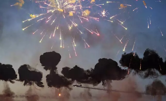 Pyrotechnics go off as the Air Bandits aerobatic team, led by Lithuanian pilot Jurgis Kairys, performs above the runway of the Aurel Vlaicu airport, at the end of the first day of the Bucharest International Air Show, BIAS, in Bucharest, Romania, Saturday, Aug. 30, 2025. (AP Photo/Andreea Alexandru)