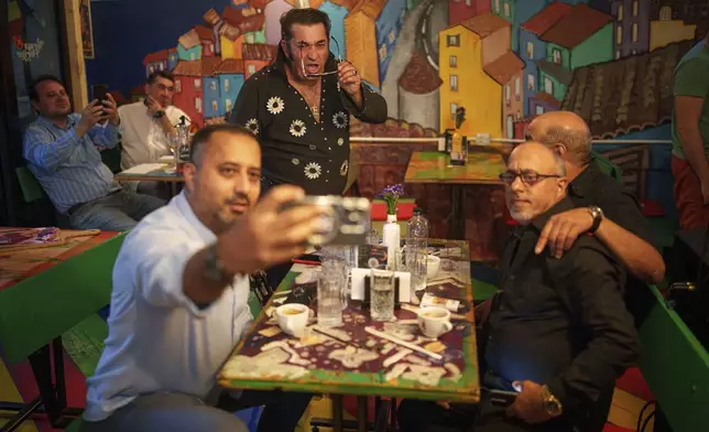 Tudor Lakatos, who goes by the stage name Elvis Rromano, strikes a pose for a photo with the Taraful Frunzelor band, Stelian Frunza, left, Stefan Marin, right, and Nicolae Feraru, at the Terasa Florilor restaurant in Bucharest, Romania, Friday, June 20, 2025. (AP Photo/Vadim Ghirda)