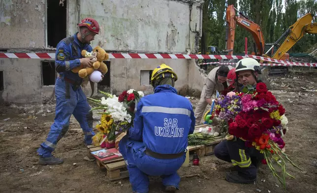 Rescuers lay toys and flowers on the site of Russia's Thursday night missile strike that hit a multistory residential house killing 31 civilians including five children in Kyiv, Ukraine, Friday, Aug. 1, 2025. (AP Photo/Efrem Lukatsky)
