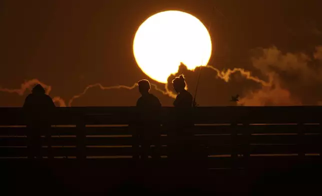 The sun rises behind a couple walking on a pier in Port Aransas, Tuesday, Aug. 12, 2025. (AP Photo/Eric Gay)
