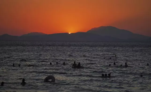 People enjoy the sea as the sun sets during a warm and windy day at Kavouri beach in southern Athens, Greece, Monday, Aug. 11, 2025. (AP Photo/Thanassis Stavrakis)
