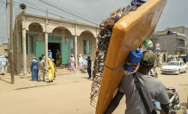 Merchantswalk past the Great Mosque of Nietty Mbar in Thiaroye, a suburb of Dakar, Senegal, Friday, July 4, 2025.(AP Photo/Sylvain Cherkaoui)