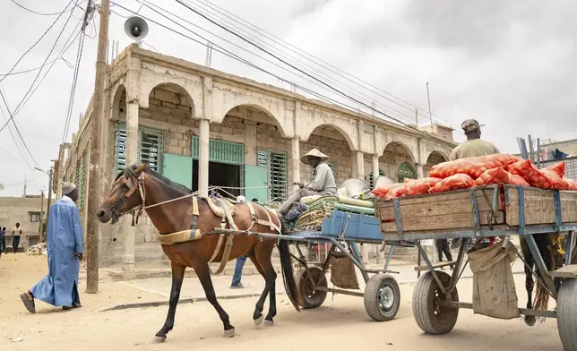 Merchants ride past the Great Mosque of Nietty Mbar in Thiaroye, a suburb of Dakar, Senegal, Friday, July 4, 2025.(AP Photo/Sylvain Cherkaoui)