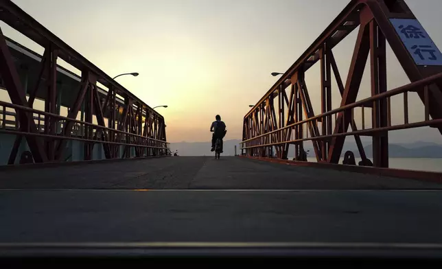 A local worker crosses the pier on a bicycle to catch a ferry in Ninoshima, an island where thousands of the dead and dying were brought after the first atomic bomb detonated 80 years ago, in western Japan, Monday, July 7, 2025. (AP Photo/Eugene Hoshiko)