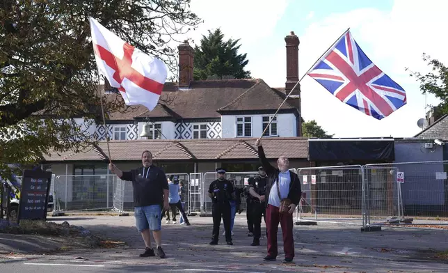 Police officers watch protesters outside the Bell Hotel in Epping, England, Friday, Aug. 29, 2025, after a temporary injunction that would have blocked asylum seekers from being housed at the hotel in was overturned at the Court of Appeal. (Lucy North/PA via AP)