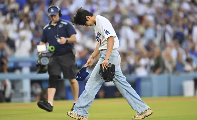 V, a member of the South Korean K-pop band BTS, takes off his cap after throwing out a ceremonial first pitch before a baseball game between the Los Angeles Dodgers and the Cincinnati Reds Monday, Aug. 25, 2025, in Los Angeles. (AP Photo/Jayne Kamin-Oncea)