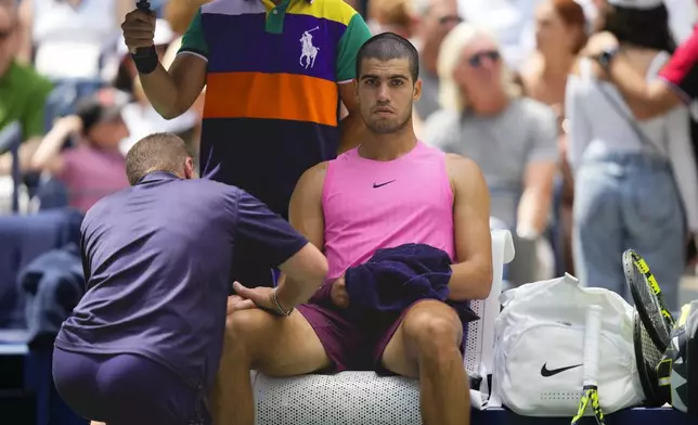 A trainer works on Carlos Alcaraz, of Spain, during a medical timeout in the second set against Luciano Darderi, of Italy, during the third round of the U.S. Open tennis championships, Friday, Aug. 29, 2025, in New York. (AP Photo/Yuki Iwamura)