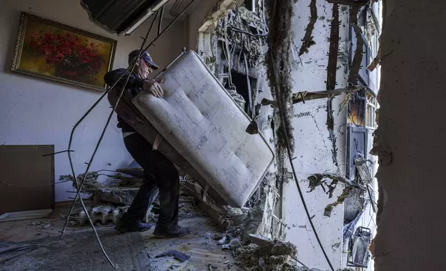 A man carries a sofa at his apartment damaged by a Russian strike in Kyiv, Ukraine, on Thursday, Aug. 28, 2025. (AP Photo/Evgeniy Maloletka)